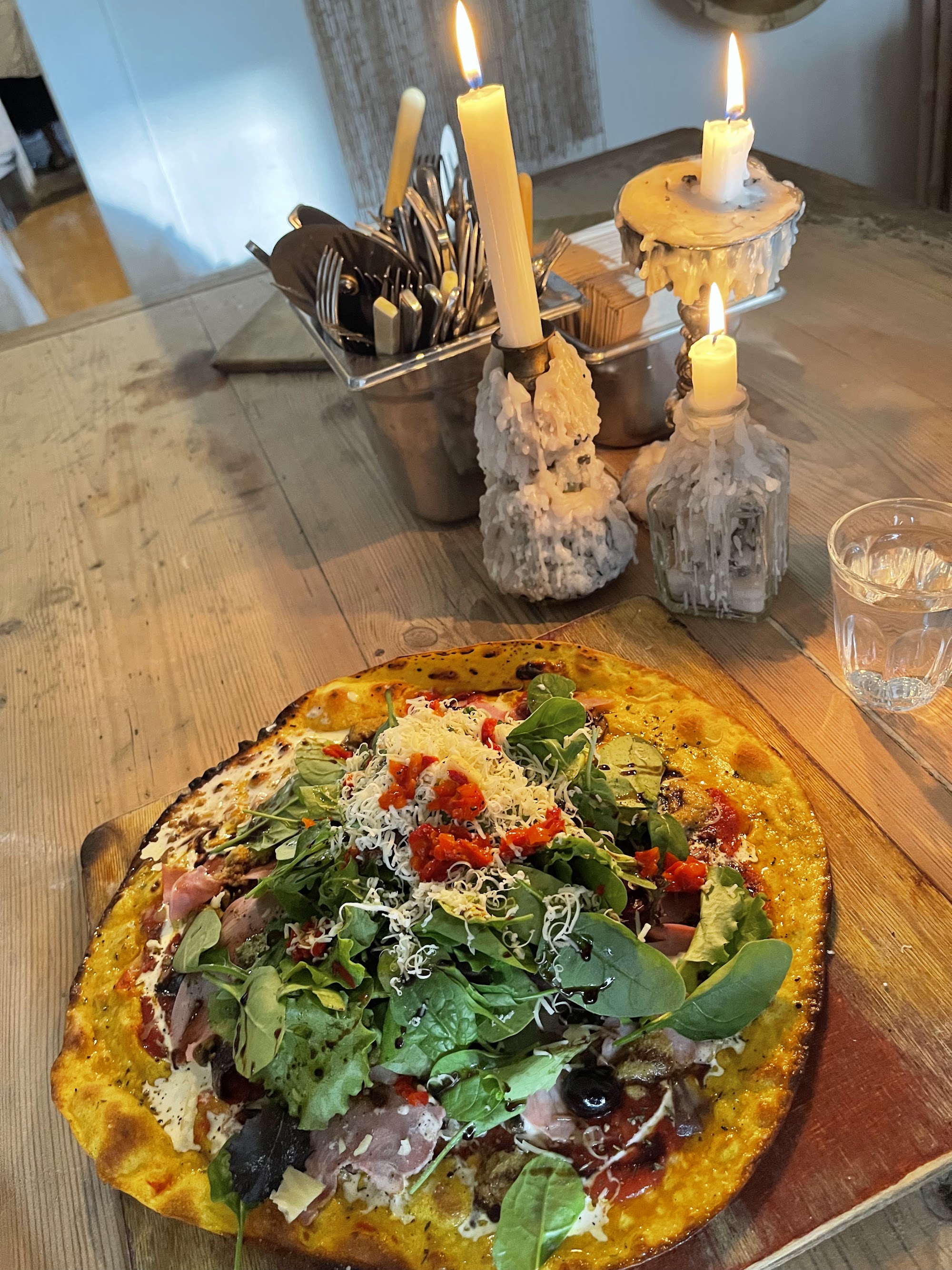A wood-fired pizza loaded with rocket, cherry tomatoes and mozzarella, lit by candlelight on a reclaimed wooden table